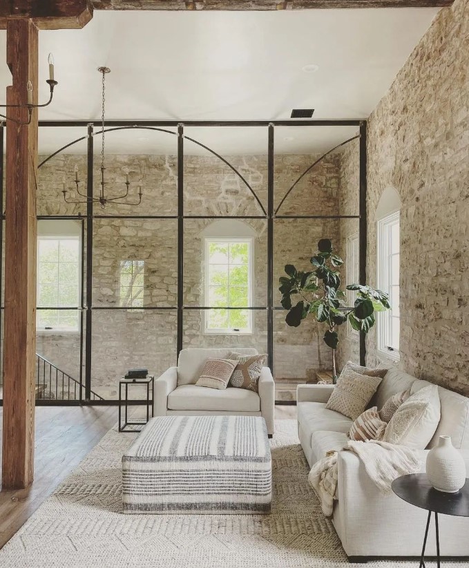 Salon dans les tons de blanc avec un mur en pierre et une verrière en fer forgée 